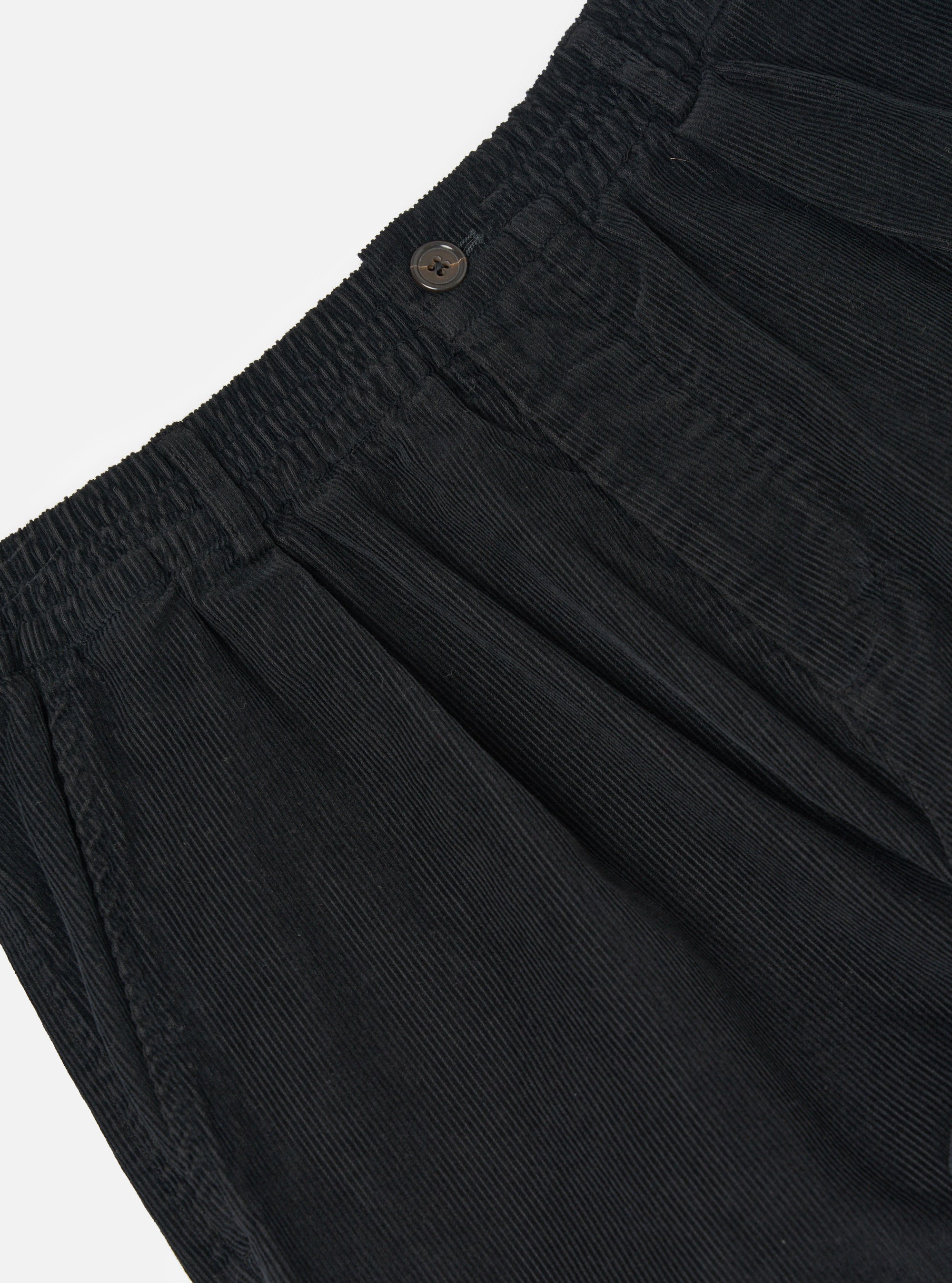 Close-up of the Black Cat Cord Pleated Track Pant, showcasing the black corduroy material, pleated design, elastic waistband, and button detail against a white background.
