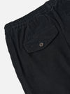 Close-up of the Black Cat Cord Pleated Track Pant, showcasing the black corduroy material, pleated design, elastic waistband, and back pocket with button closure on a white background.