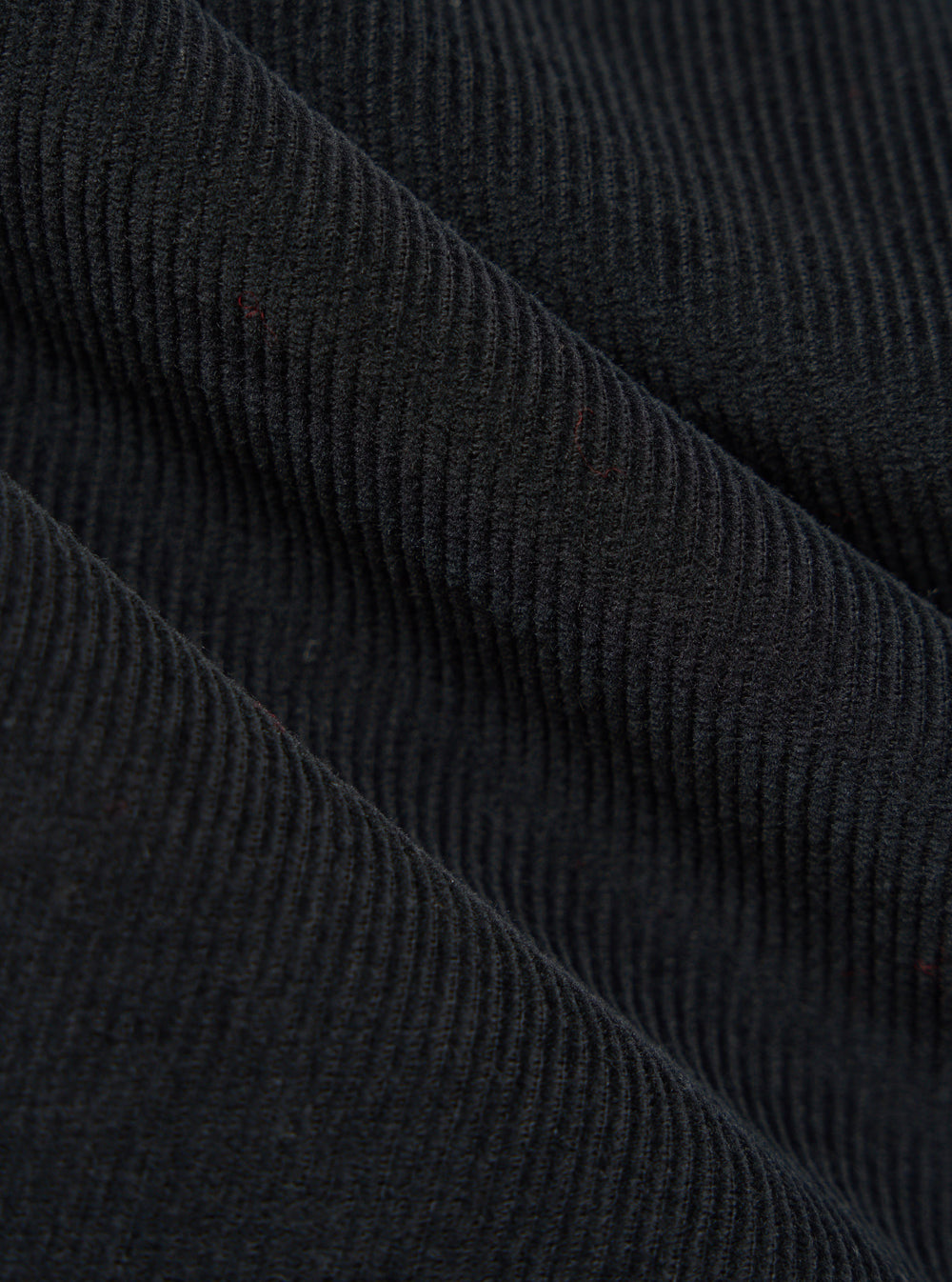 Close-up of the Black Cat Cord Pleated Track Pant fabric. The black corduroy material is draped to show its texture and pleats. 