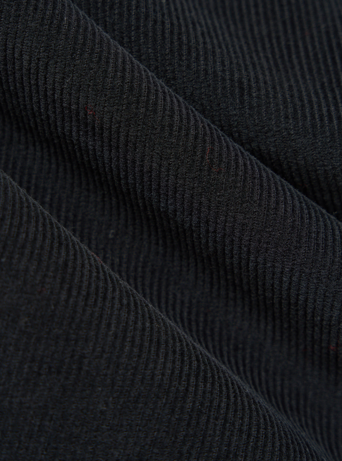 Close-up of the Black Cat Cord Pleated Track Pant fabric. The black corduroy material is draped to show its texture and pleats. 