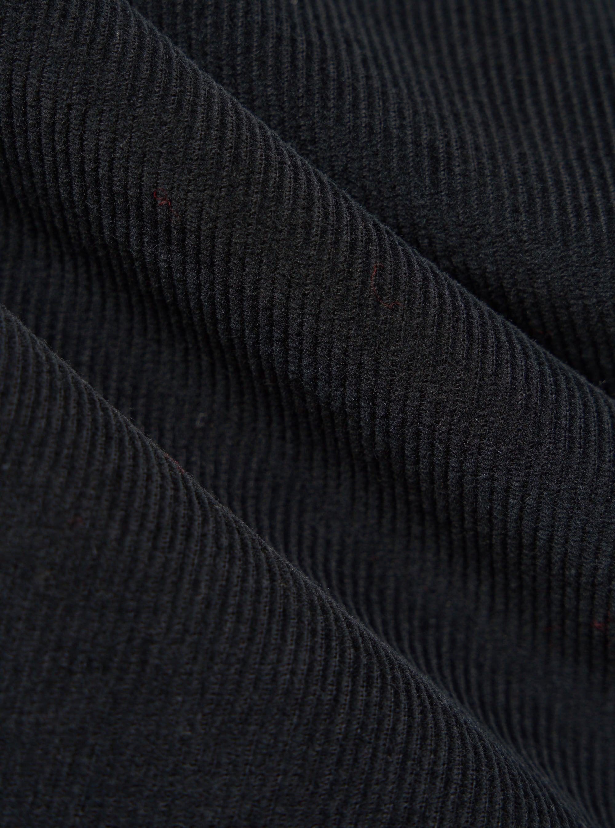 Close-up of the Black Cat Cord Pleated Track Pant fabric. The black corduroy material is draped to show its texture and pleats. 