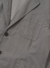 The Mid Grey Linen Slub Weave Two Button Jacket is shown as a flat lay against a white background. The jacket features a two-button front closure, a notched collar, and two large patch pockets at the hips. The fabric has a visible slub texture in a mid-grey tone.