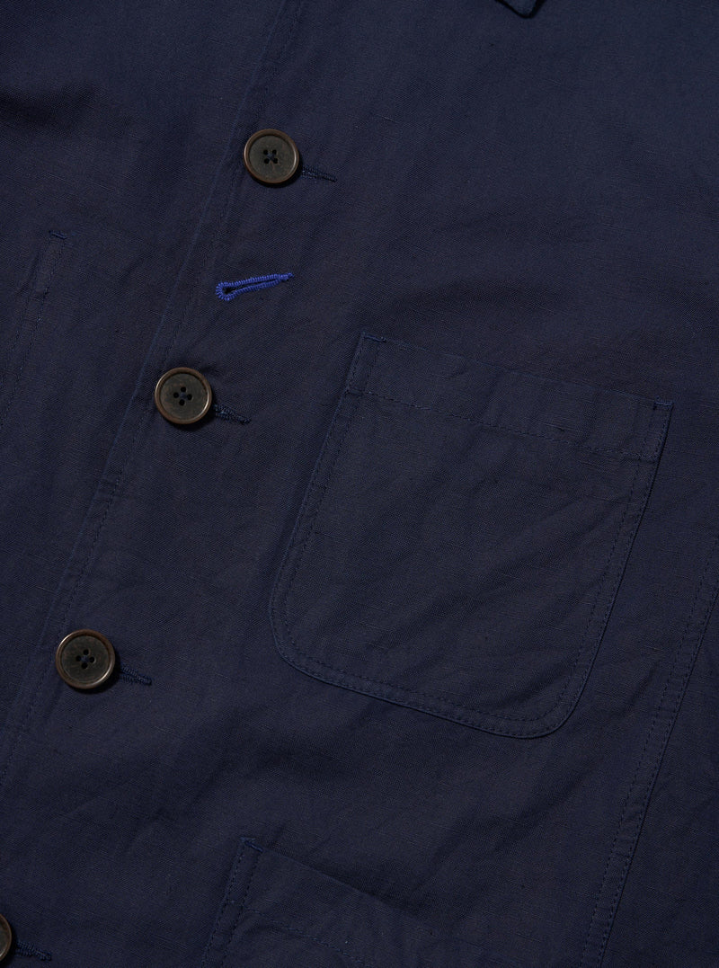 The Navy Linen Slub Weave Bakers Jacket is shown from the back, laid flat against a solid white background. The image highlights the textured navy blue linen-cotton blend fabric, featuring a two-piece sleeve construction and a centered back vent.