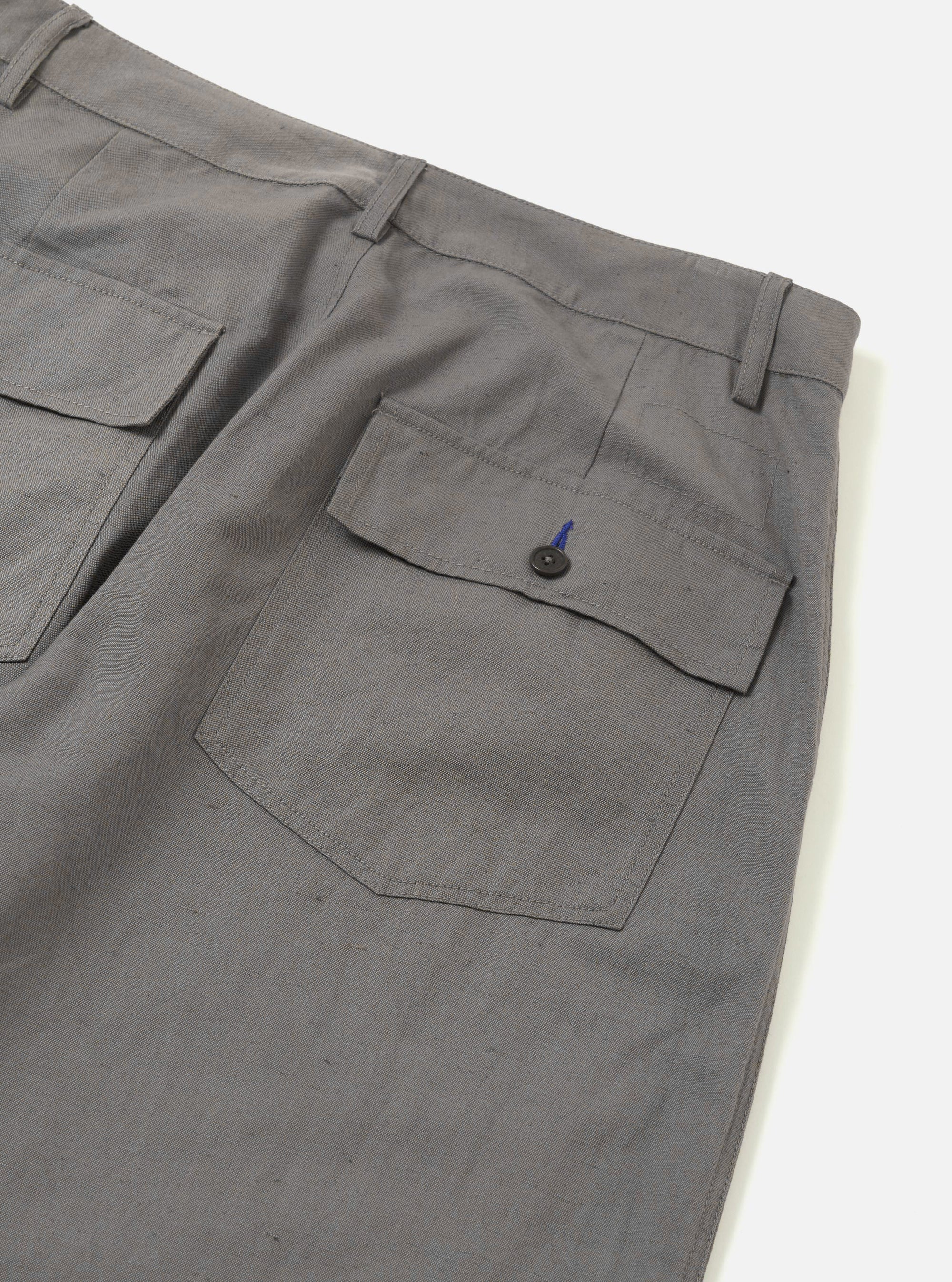 The Mid Grey Linen Slub Weave Dizzy Trouser is shown from the back as a flat lay against a plain white background. The image highlights the two rear pockets, including one with a buttoned flap and one buttoned jetted pocket, as well as the elasticated waistband. The mid grey fabric features a visible slub weave texture.
