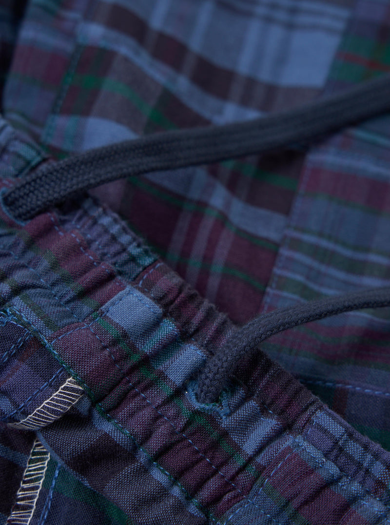 A pair of navy madras patchwork vacation shorts is displayed flat against a plain white background. The shorts feature a patchwork design of various blue and navy plaid fabrics, an elasticated waistband, and a rear patch pocket.