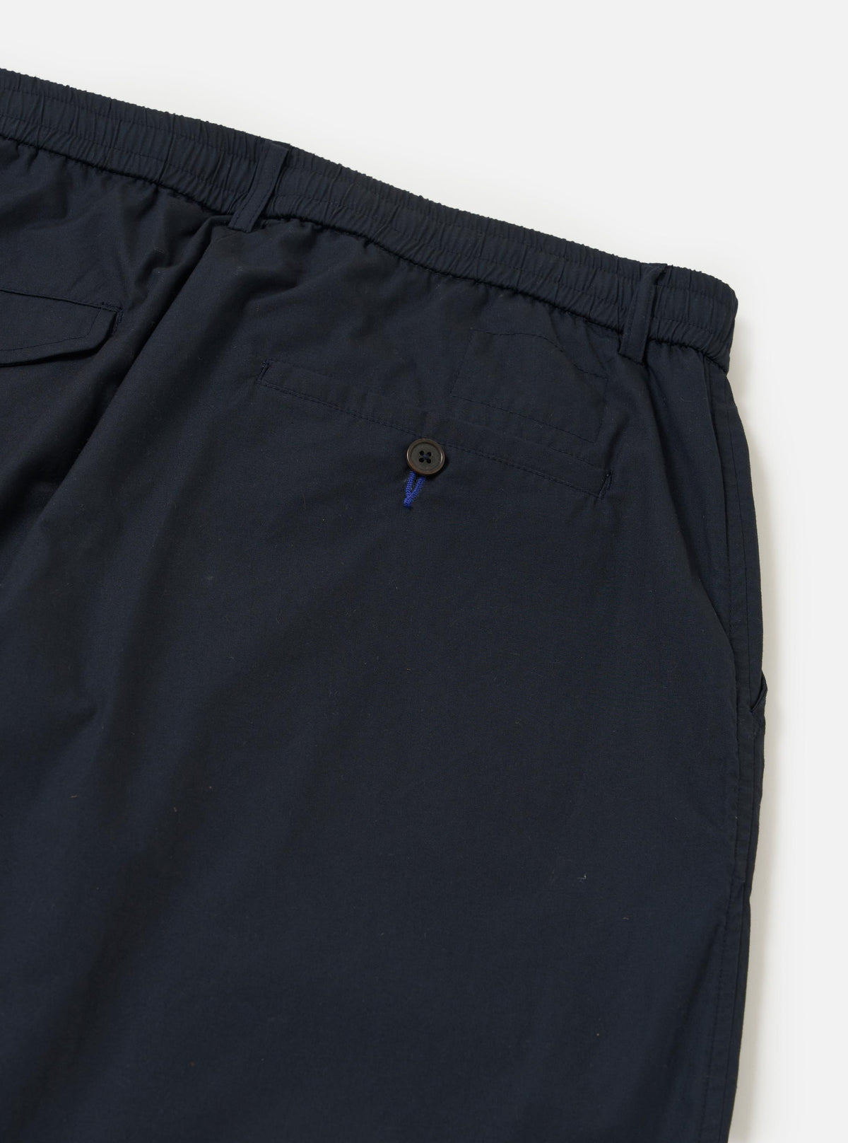 A rear view of the Navy Broadcloth Oxford Pant is displayed flat against a plain white background. The image highlights the waistband and a single rear buttoned flap pocket on the dark navy fabric.