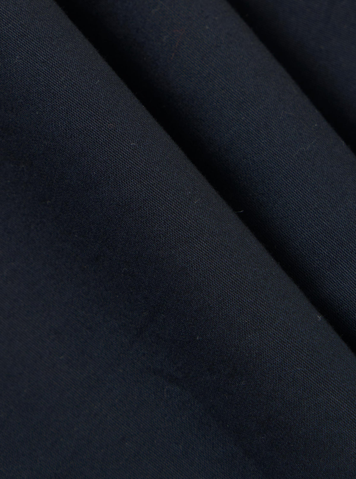 A close-up fabric swatch of the Navy Broadcloth Oxford Pant shows a detailed view of the navy blue material. The image highlights the smooth, tightly woven texture of the broadcloth fabric against a neutral background.