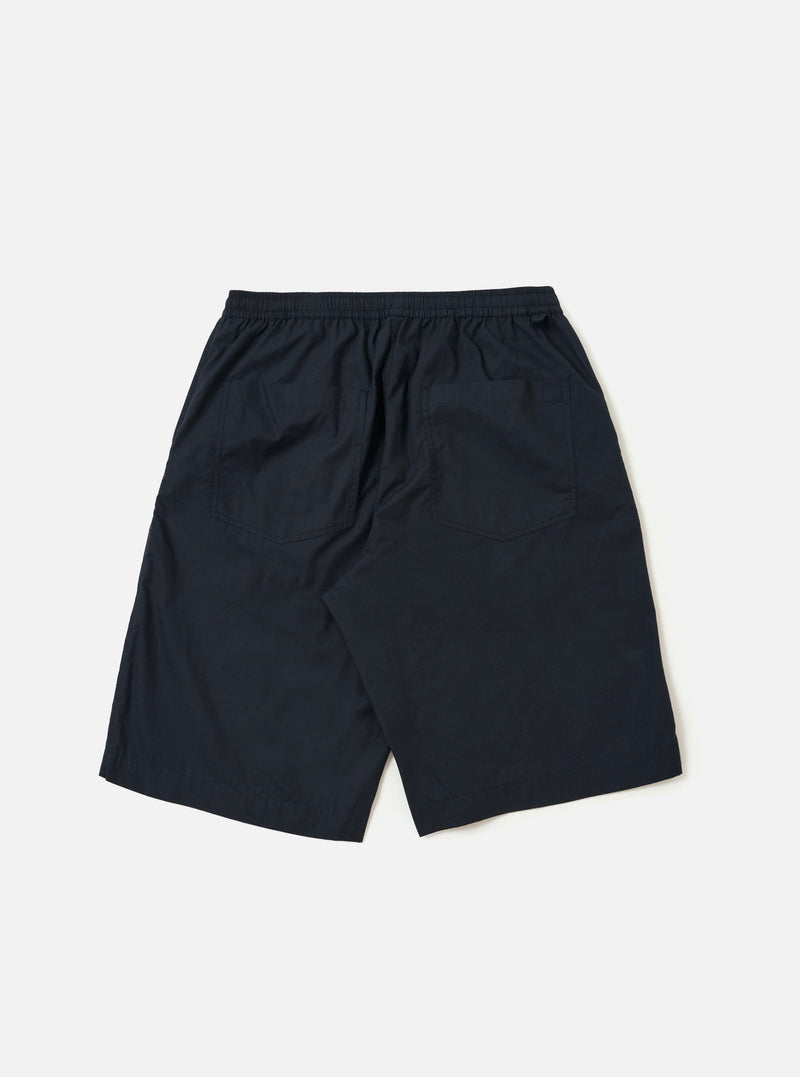 The Navy Broadcloth Vacation Short is shown from a rear angle, laid flat against a plain white background. The image highlights the lightweight navy blue cotton fabric, an elasticated waistband, and a single rear patch pocket on the right side.