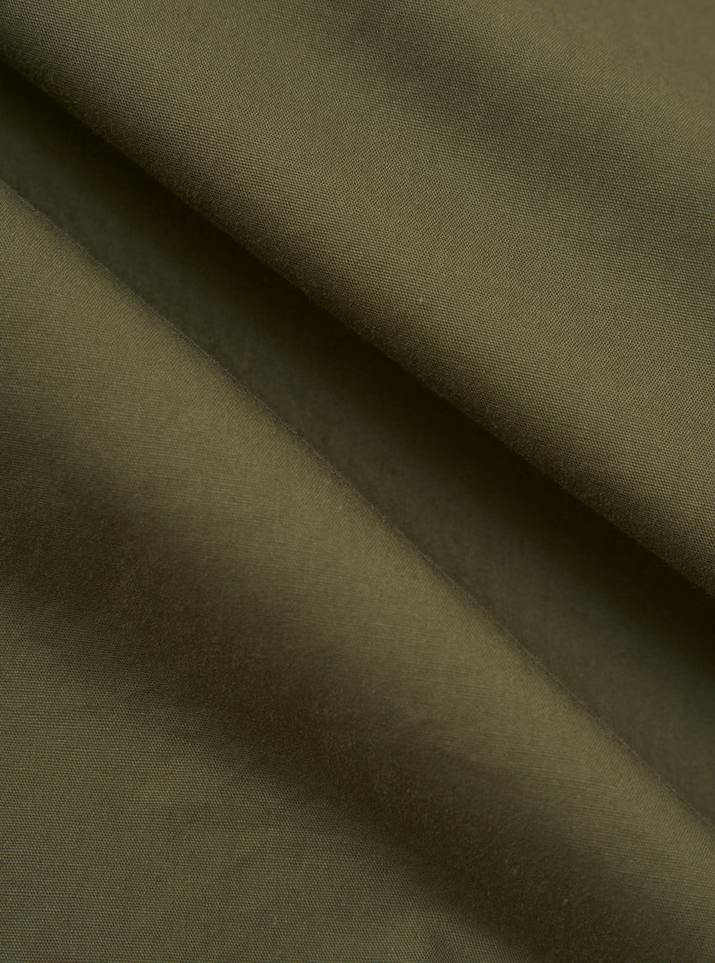 A close-up fabric swatch of the Olive Broadcloth Vacation Short displays the smooth, tight weave of the olive green cotton broadcloth. The image focuses on the uniform color and texture of the material.