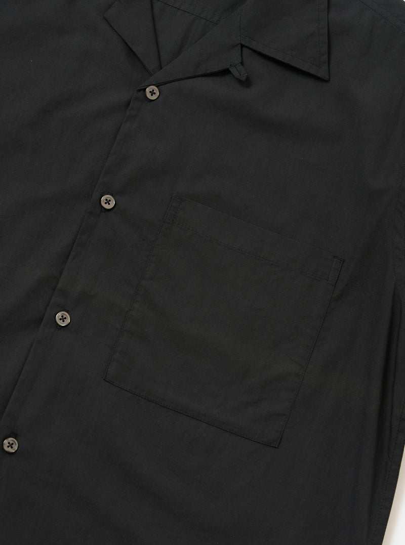 A Black Broadcloth Camp Shirt is displayed flat against a plain white background. The shirt features a classic camp collar, a full button-down front, and short sleeves. The fabric is a smooth black cotton broadcloth.