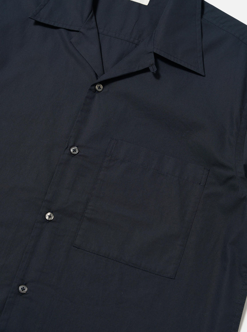 The Navy Broadcloth Camp Shirt is shown from the back, laid flat against a plain white background. The image highlights the back yoke with small pleats and the elongated hem which is longer at the back with side splits.