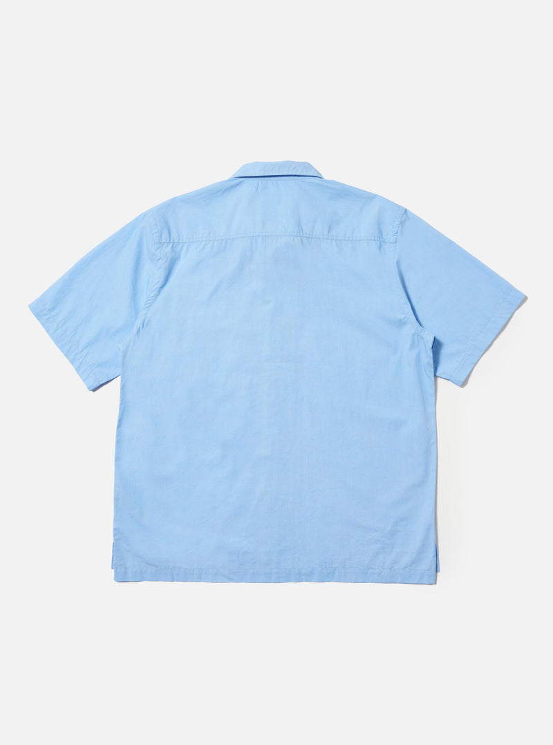 A Pale Blue Broadcloth Camp Shirt is shown from the back, laid flat against a plain white background. The image prominently features the back yoke with small pleats and a straight, even hem.