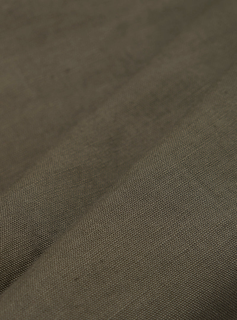A detailed, close-up fabric swatch of the olive green linen-cotton shirting material used for the Bakers Overshirt. The image highlights the textured weave and solid color of the fabric.