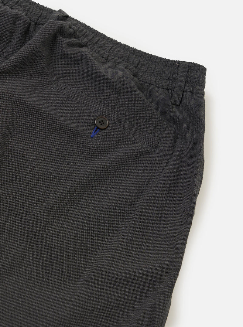A close-up view of the back of the Charcoal Seattle Cotton Pleated Track Pant focuses on the waistband and two rear pockets. One pocket is a buttoned jetted style, while the other features a buttoned flap. The charcoal grey cotton fabric is shown against a plain white background.