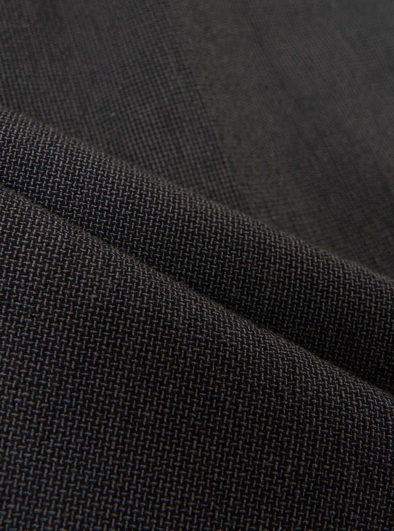 A detailed, close-up fabric swatch of the charcoal grey Seattle cotton material used for the Pleated Track Pant. The image highlights the fine basket weave and textured surface of the cotton fabric.
