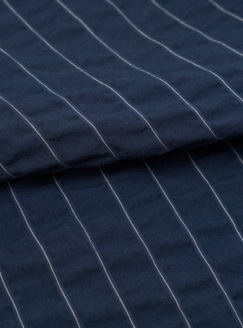 A close-up fabric swatch of the Navy Chester Stripe Oxford Pant is shown against a plain white background. The image highlights the fine vertical pinstripe pattern on the navy blue cotton fabric, showcasing the material's texture and detail.