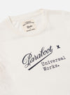 Close-up of the Paraboot x Universal Works Ecru Single Jersey Short Sleeve Tee. The ecru tee features a collab logo. Laid flat on a white surface.