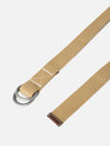 Close-up of a Sand Canvas O Ring Belt on a white background. The belt is made of canvas with a sand color and has an O-ring buckle. The end of the belt has a brown leather tip.
