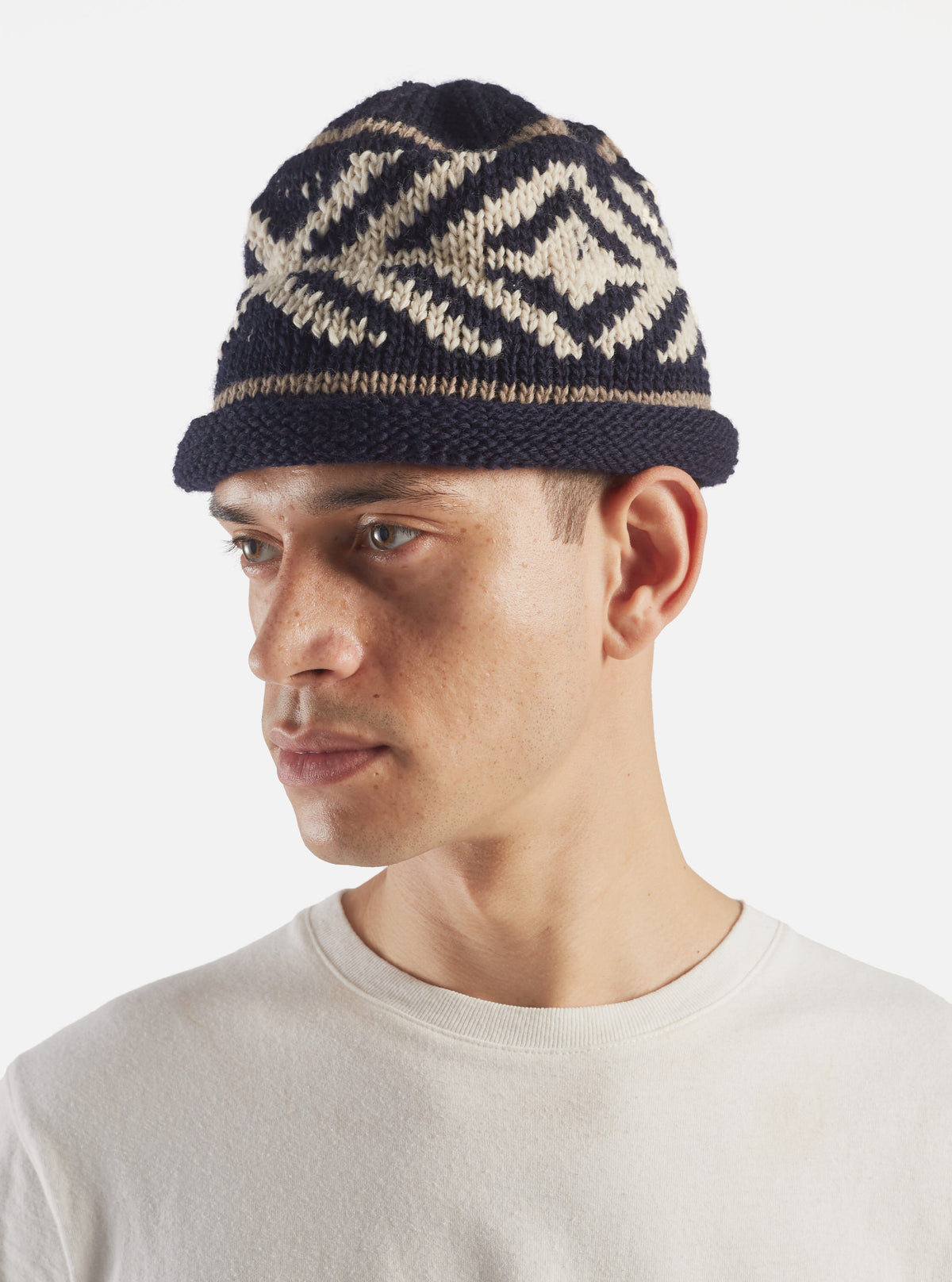 A close-up detail shot of the cableami® Navy Wool Jacquard Watch Cap against a white background, emphasizing the intricate jacquard weave texture, fine wool yarn construction, and folded cuff seam.
