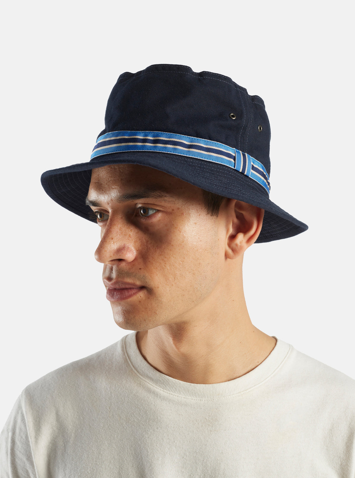 A model wears the cableami® Navy Chino Cotton Loose Light Pork Pie Hat. The hat is navy with a blue striped band. Shot on a white background.