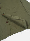 Close-up of a light olive twill Bakers Jacket on a white surface. The jacket features brown buttons and visible stitching details.