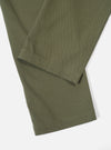 Close-up of the Light Olive Twill Aston Pant on a white surface. The twill fabric is a light olive color. The hem is neatly stitched.