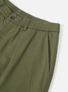 Close-up of the light olive twill pleated track pant on a white background. Details include the elastic waistband, button, and pocket.
