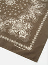 Close-up of an Olive Classic Bandana Neckerchief on a white surface. The bandana is olive green with a white floral and paisley pattern. The corner shows the brand name.