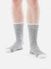 A person stands on a white background wearing Grey Marl Alpaca Wool Sock. The socks are grey with white toes and white trim at the top.