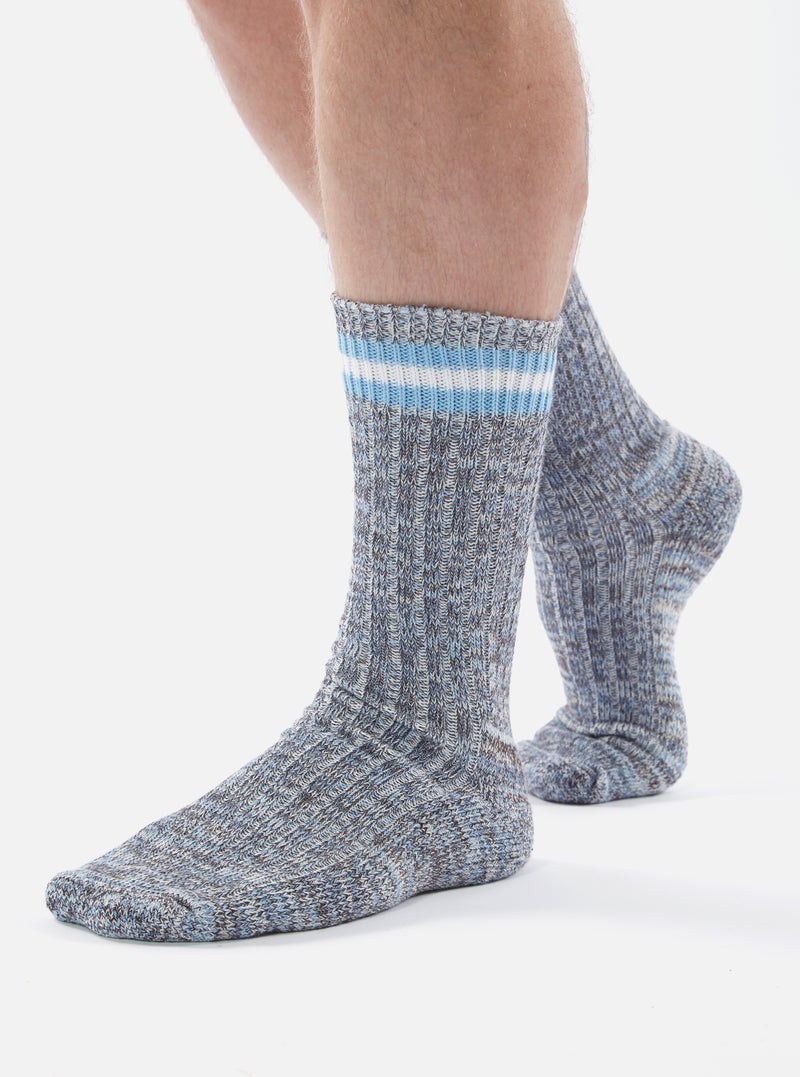 Close up of a model wearing Cornish Blue Cotton Everyday Stripe Sock on a white background. The sock is blue with white and light blue stripes at the top.