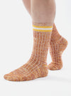 A model wears Yellow Cotton Everyday Stripe Sock on a white background. The socks have yellow and white stripes at the top and are made of a textured cotton blend.