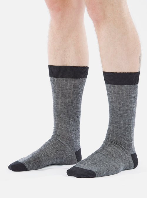 Close-up of a model wearing Grey Marl Merino Classic Sock. The sock is grey with a black toe and top. The background is a plain white.