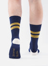 Close-up of a model wearing Navy/Yellow Cotton Rib Sport Sock against a white background. The sock is navy with yellow stripes and a white heel.