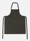 Studio shot of a Black Selvedge Denim Apron on a white background. The apron has black straps and multiple pockets.