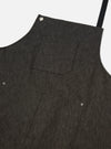 Close-up of a Black Selvedge Denim Apron on a white background. The apron has pockets and black straps.