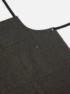 Close-up of a Black Selvedge Denim Apron on a white background. The apron has black straps and a small pocket. The selvedge edge is visible with a red line.