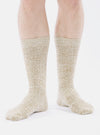 A model stands against a white backdrop, showcasing the Dark Sand Slub Knit Slub Sock. The socks are a textured, light tan color and reach mid-calf.
